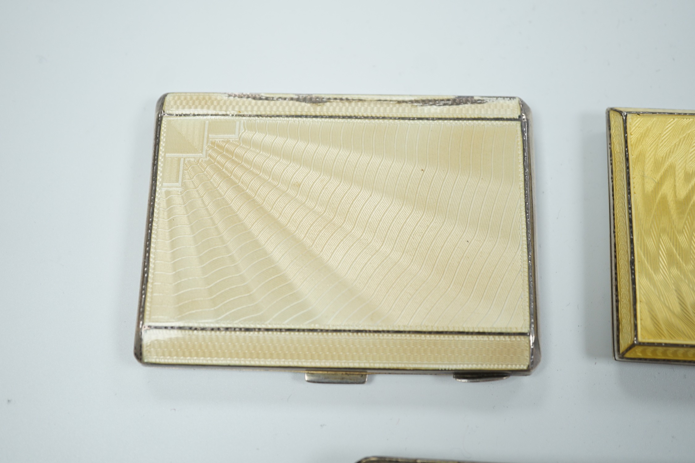 Two George V Art Deco silver and enamel cigarette cases, Birmingham, 1931 & 1932, largest 85mm (enamel a.f. on one) together with a German 800 standard white metal, cabochon emerald and rose cut diamond set compact/minau